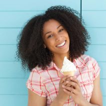 Close up portrait of a beautiful young black woman smiling with ice cream on blue background